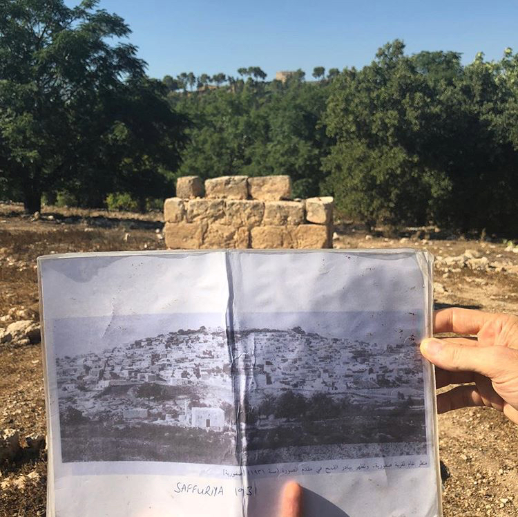 A picture of the fields where a demolished village lay, with a book in front with a picture of the village as it looked in 1931